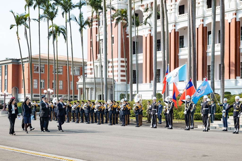 Upon arrival, the ambassador steps out of the vehicle in front of gate two of the Presidential Office Building and then reviews the honor guard and band